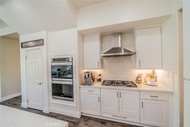 kitchen with stainless steel appliances, wall chimney range hood, tasteful backsplash, light countertops, and white cabinets