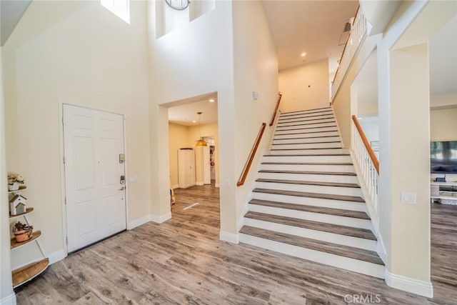 foyer entrance featuring recessed lighting, baseboards, wood finished floors, stairway, and a high ceiling