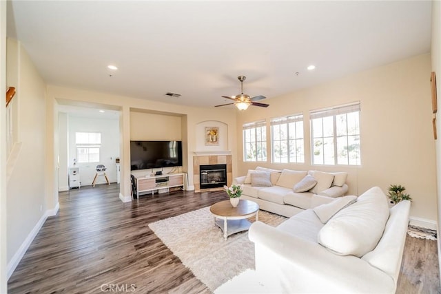 living room with a ceiling fan, baseboards, dark wood finished floors, visible vents, and a tile fireplace
