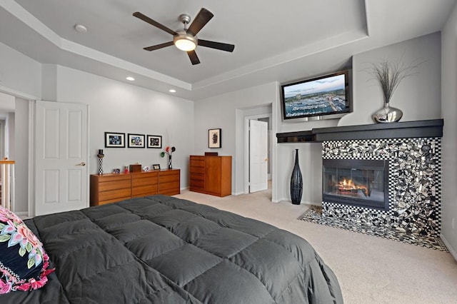 bedroom featuring a ceiling fan, recessed lighting, carpet, a tiled fireplace, and a raised ceiling