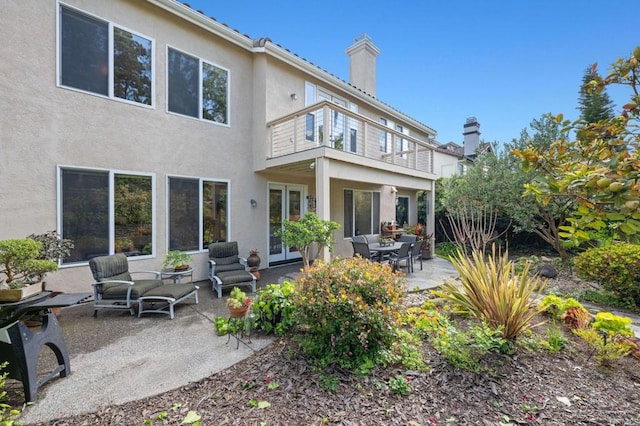 rear view of house featuring a balcony, a chimney, french doors, a patio area, and stucco siding