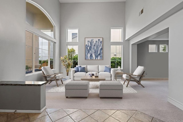 living room with visible vents, a towering ceiling, a healthy amount of sunlight, and light carpet