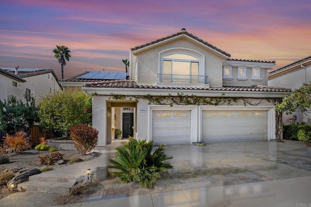 view of front of property featuring driveway, a tile roof, a garage, stucco siding, and solar panels
