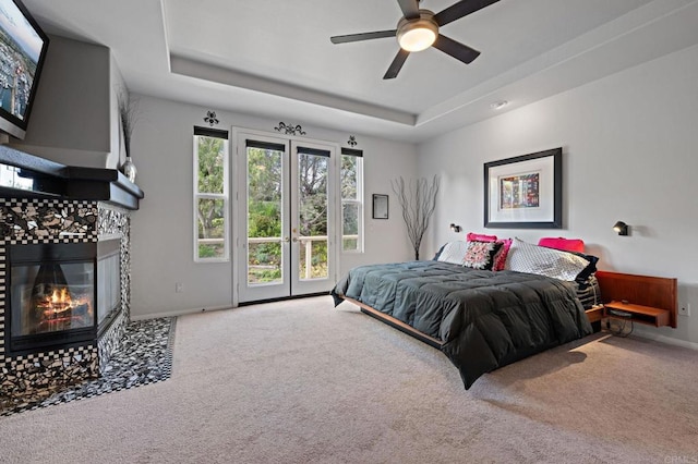 carpeted bedroom featuring baseboards, a tile fireplace, a tray ceiling, and access to exterior