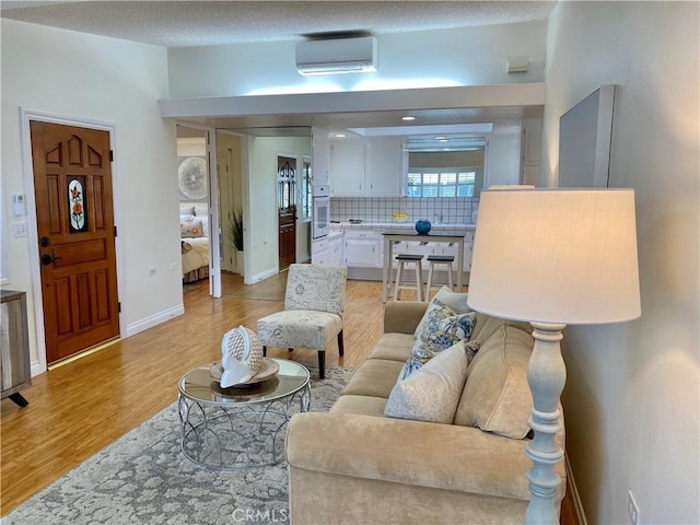 living room with baseboards, a wall mounted air conditioner, and light wood-type flooring