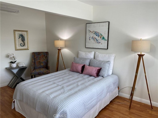 bedroom with baseboards, a wall unit AC, and wood finished floors