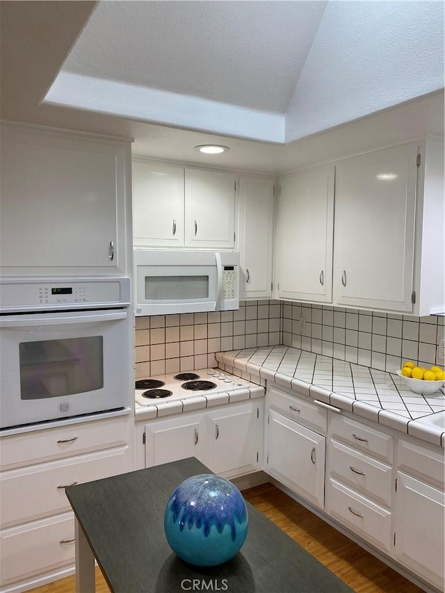 kitchen with white cabinetry, white appliances, tile counters, and backsplash