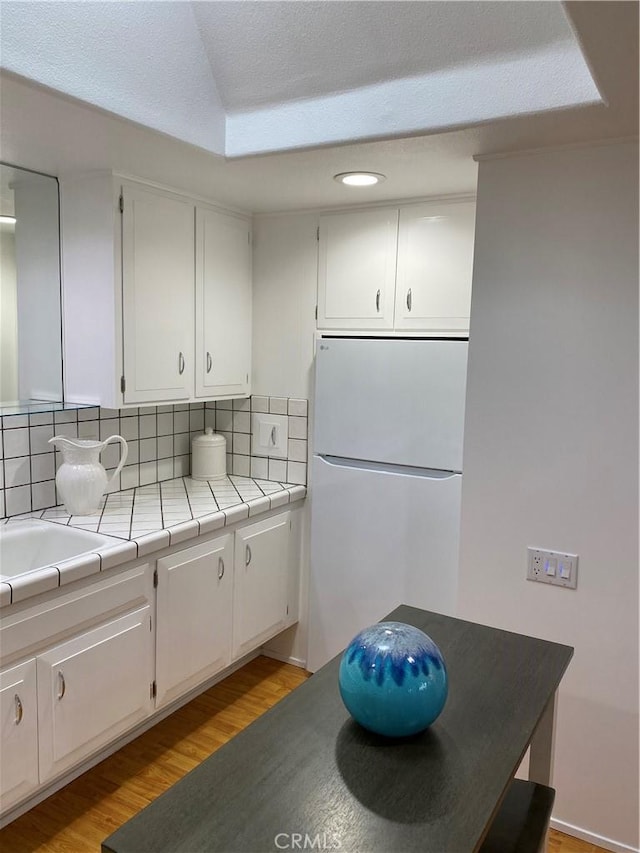 kitchen featuring freestanding refrigerator, backsplash, white cabinets, and light wood-type flooring