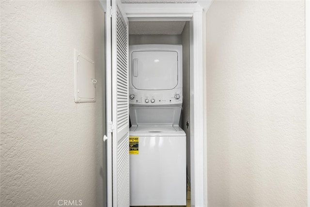 washroom featuring stacked washer and clothes dryer and a textured wall