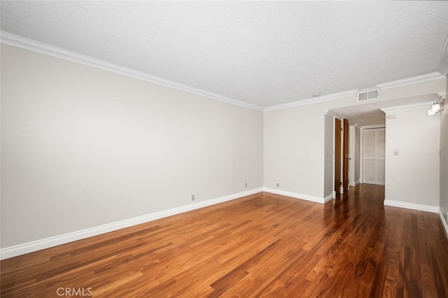 spare room with a textured ceiling, wood finished floors, ornamental molding, and baseboards