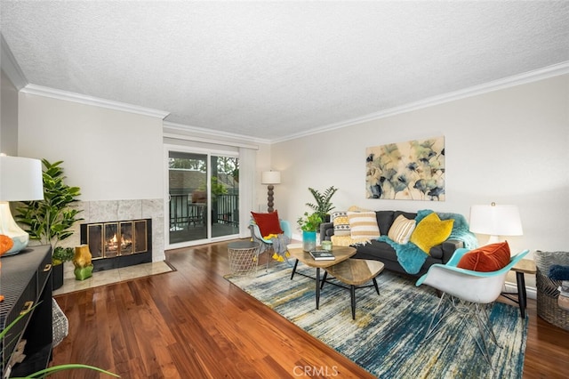 living area featuring wood finished floors, crown molding, a textured ceiling, and a tiled fireplace