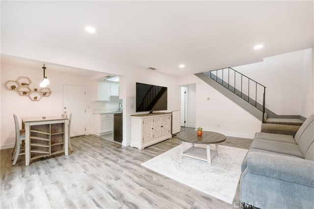 living room featuring recessed lighting, light wood-style flooring, baseboards, and stairs
