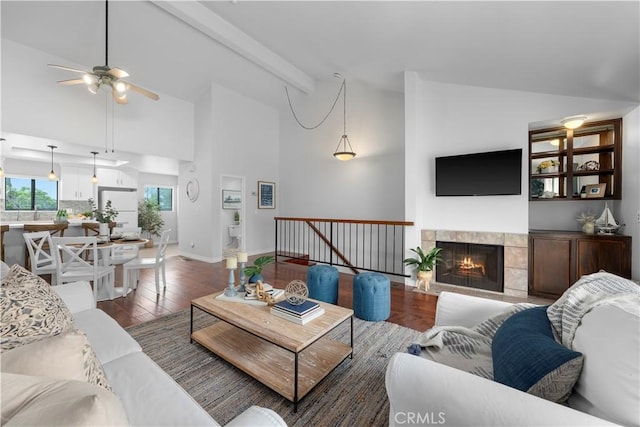 living area with a ceiling fan, high vaulted ceiling, wood finished floors, beamed ceiling, and a fireplace