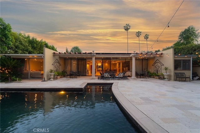 back of house at dusk with a patio and an outdoor pool