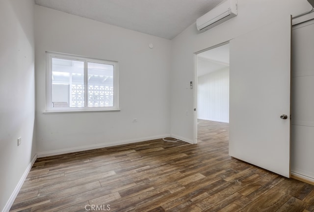 unfurnished room with a wall mounted AC, baseboards, and wood finished floors