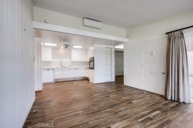 kitchen with a sink, dark wood finished floors, dishwasher, an AC wall unit, and white cabinetry