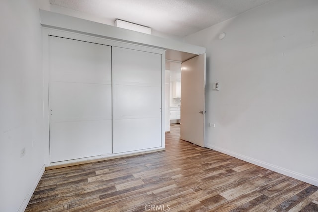 unfurnished bedroom with a textured ceiling, a closet, baseboards, and wood finished floors