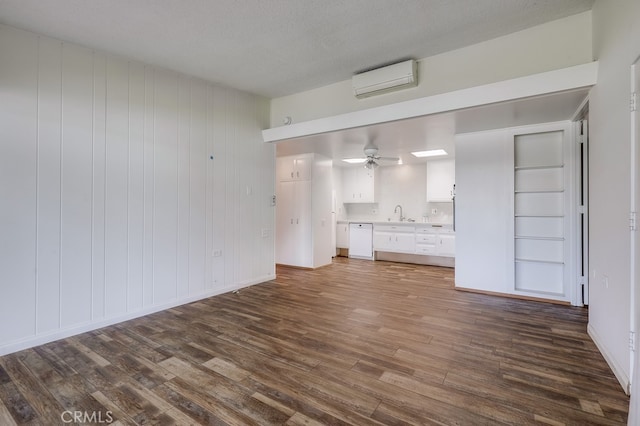 unfurnished living room with a sink, an AC wall unit, a ceiling fan, and dark wood finished floors