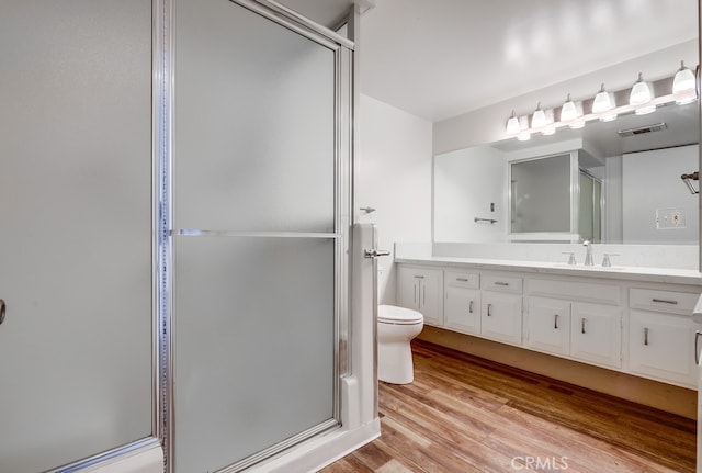 bathroom with toilet, wood finished floors, a stall shower, visible vents, and vanity