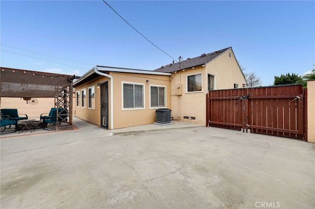 rear view of property with fence, central AC, a patio area, stucco siding, and a gate