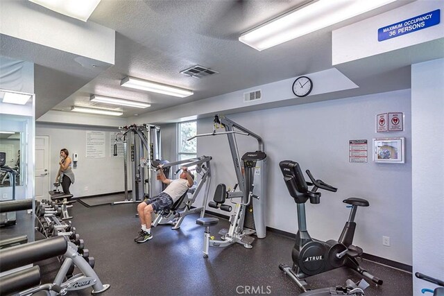 gym featuring a textured ceiling and baseboards