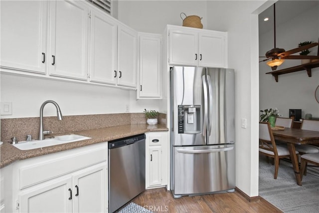 kitchen with stainless steel appliances, a sink, white cabinets, wood finished floors, and light stone countertops