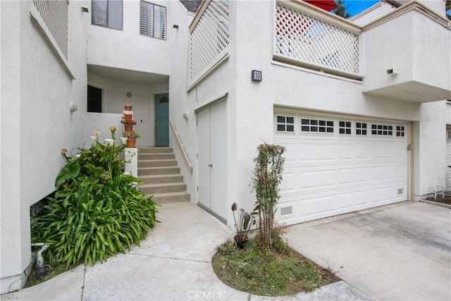 doorway to property featuring stucco siding, an attached garage, and driveway