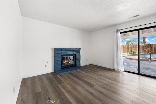 unfurnished living room with wood finished floors, a fireplace, a textured ceiling, visible vents, and baseboards