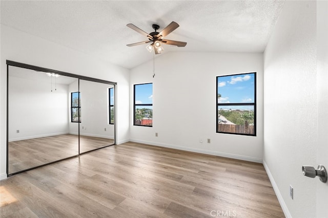 unfurnished bedroom with vaulted ceiling, light wood-style flooring, a textured ceiling, and baseboards
