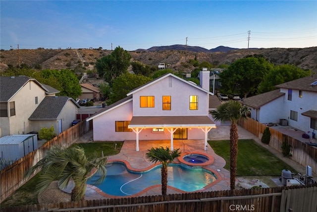 back of property with a mountain view, a patio area, stucco siding, an in ground hot tub, and a fenced backyard