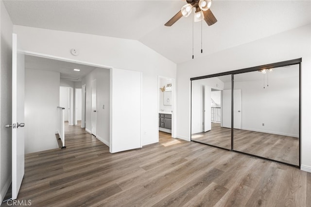 unfurnished bedroom with a closet, wood finished floors, ensuite bath, vaulted ceiling, and a ceiling fan