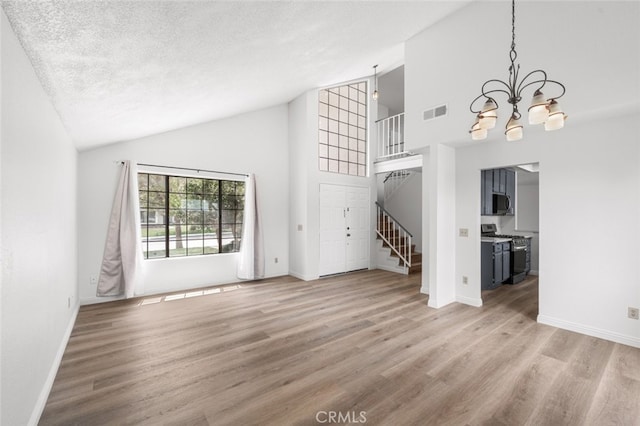 unfurnished living room with a chandelier, stairs, visible vents, and wood finished floors