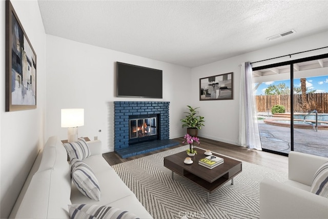 living area with wood finished floors, a textured ceiling, visible vents, a brick fireplace, and baseboards