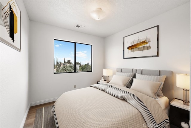 bedroom with baseboards, visible vents, and wood finished floors