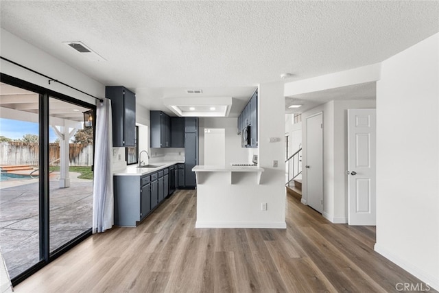 kitchen featuring a textured ceiling, visible vents, stainless steel microwave, light countertops, and light wood-style floors