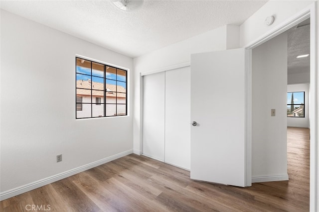 unfurnished bedroom featuring baseboards, a closet, a textured ceiling, and wood finished floors