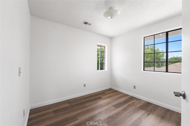 unfurnished room featuring a textured ceiling, visible vents, wood finished floors, and baseboards