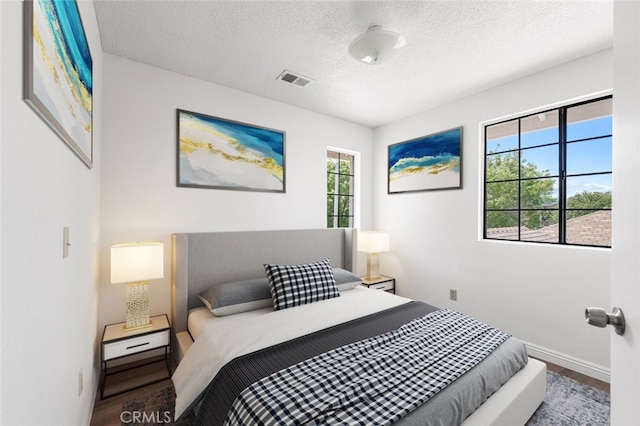 bedroom featuring a textured ceiling, baseboards, visible vents, and wood finished floors