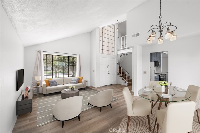living room with stairs, wood finished floors, high vaulted ceiling, visible vents, and an inviting chandelier
