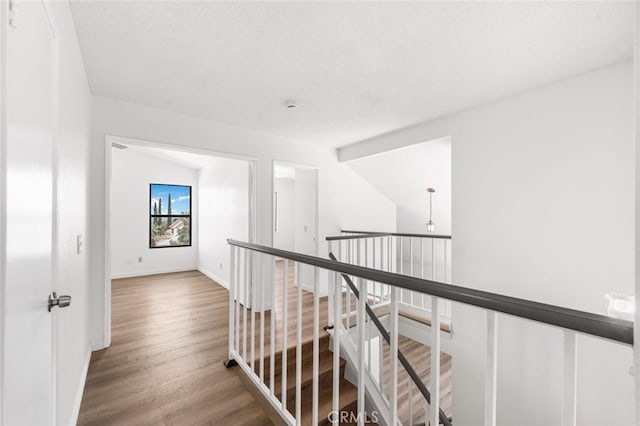 hall with baseboards, an upstairs landing, and wood finished floors