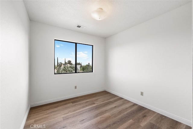 spare room featuring baseboards, visible vents, and wood finished floors