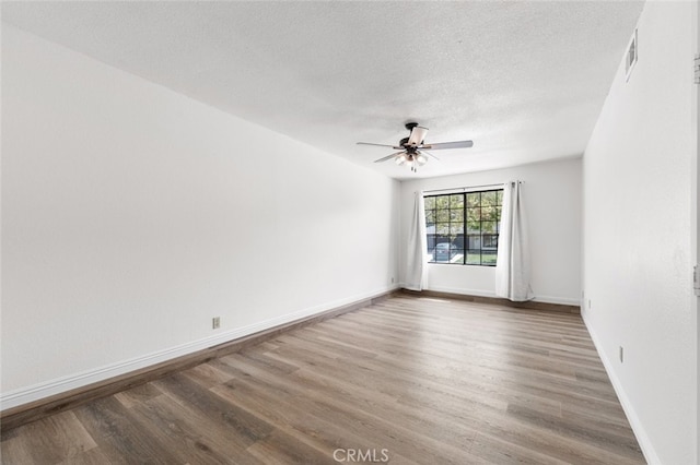 empty room with a textured ceiling, a ceiling fan, visible vents, and wood finished floors