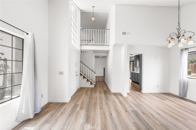 unfurnished living room featuring stairway, visible vents, a high ceiling, and wood finished floors