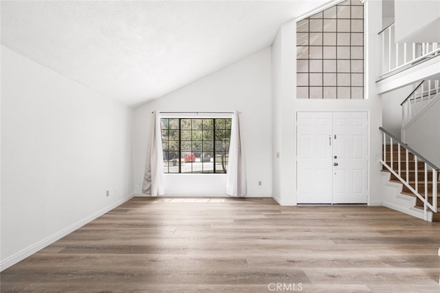 interior space featuring baseboards, stairs, high vaulted ceiling, and wood finished floors