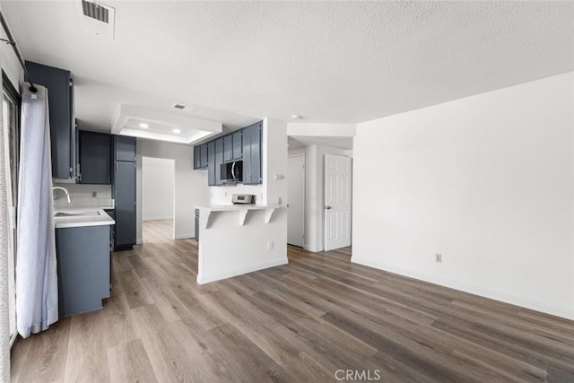 kitchen featuring a textured ceiling, stainless steel microwave, a peninsula, wood finished floors, and light countertops