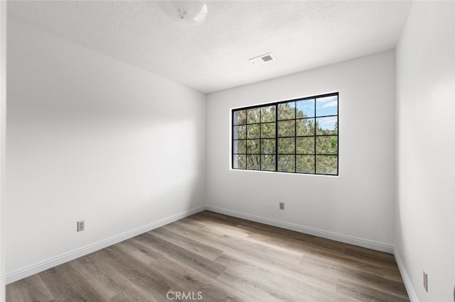 empty room with baseboards, visible vents, a textured ceiling, and wood finished floors
