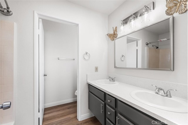 full bathroom with a sink, double vanity, toilet, and wood finished floors