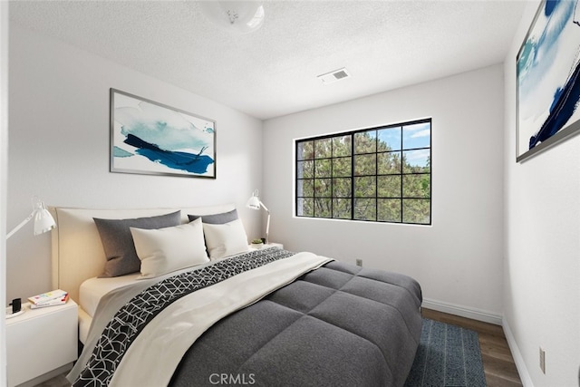 bedroom with baseboards, visible vents, a textured ceiling, and wood finished floors