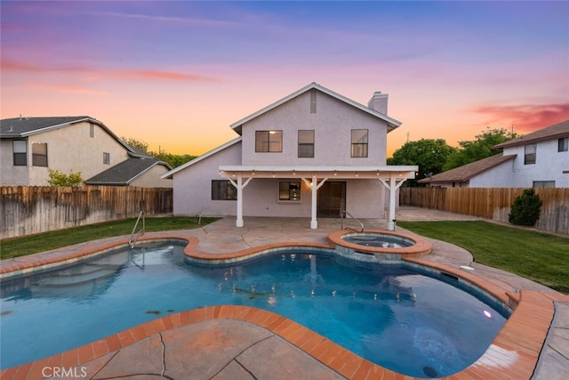 pool at dusk featuring a yard, a patio area, a pool with connected hot tub, and a fenced backyard
