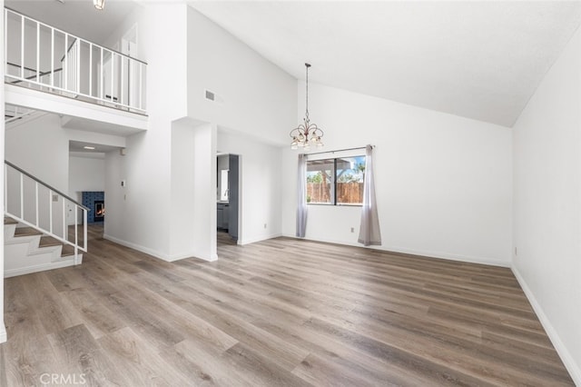 unfurnished living room featuring stairs, wood finished floors, high vaulted ceiling, an inviting chandelier, and baseboards